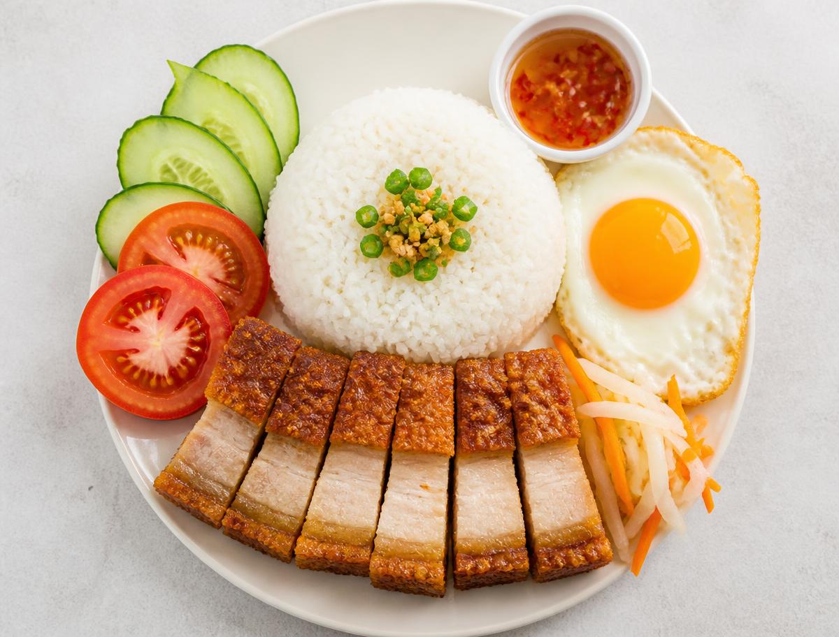 Crispy pork belly rice plate with jasmine rice, cucumber, tomato, pickles and fried egg